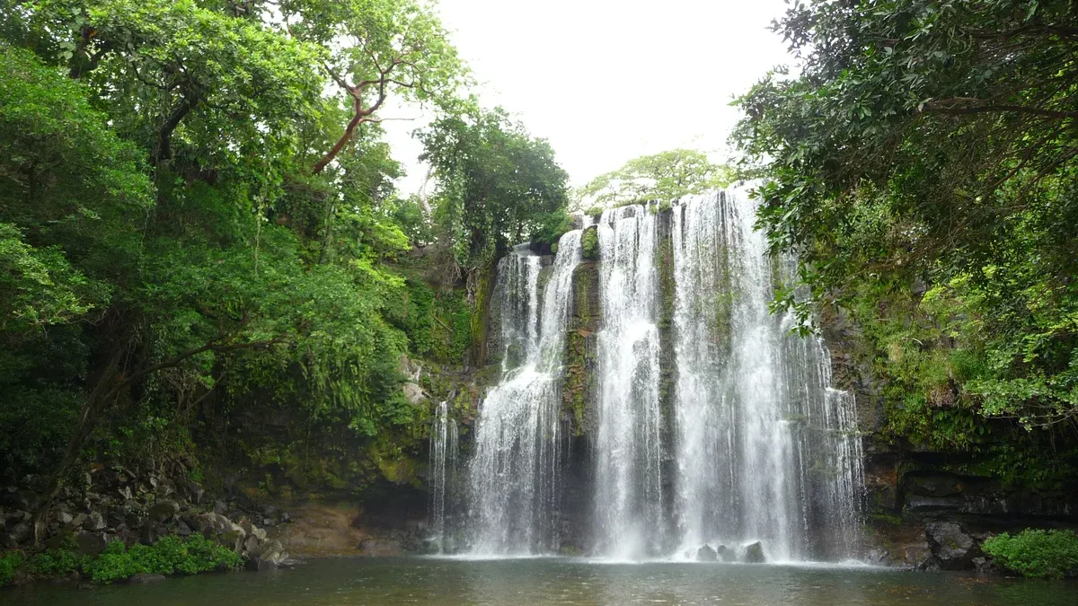 Llanos de Cortes waterfall with a wide sandy bank on the Rio Celeste and sloth sanctuary tour from Guanacaste, Costa Rica